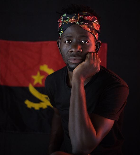 Man posing with a thoughtful expression in front of an Angolan flag, Luanda, Angola.