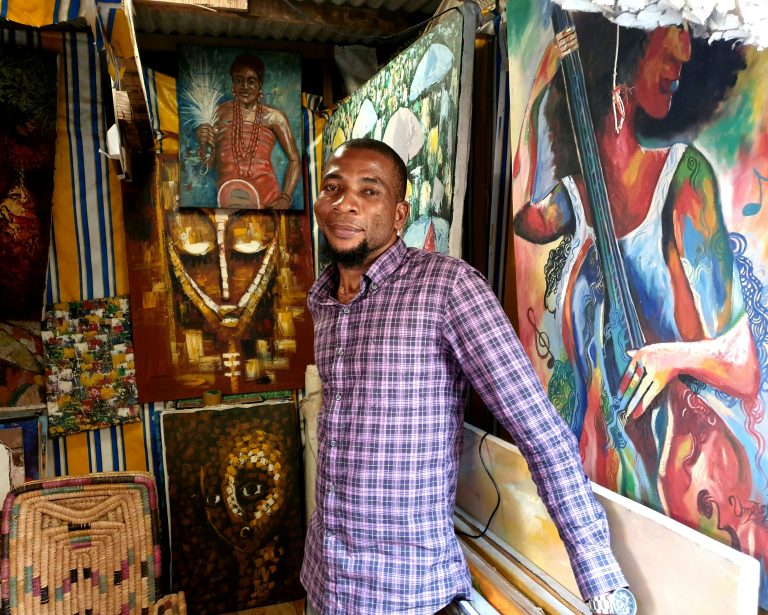 Art dealer surrounded by colourful works at Lekki Arts and Crafts Market in Lagos
