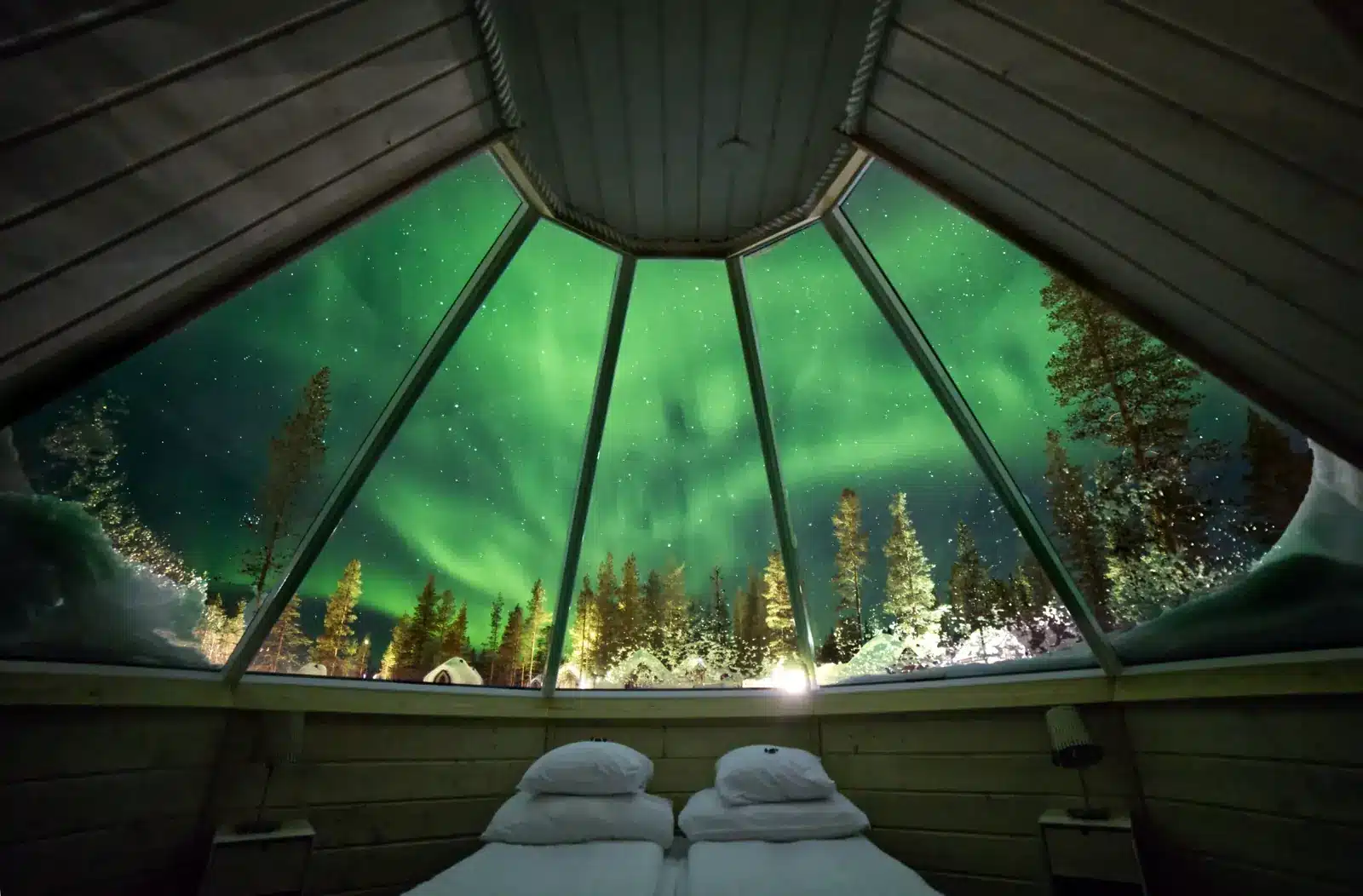 Northern Lights seen through a glass-roof cabin above a double bed