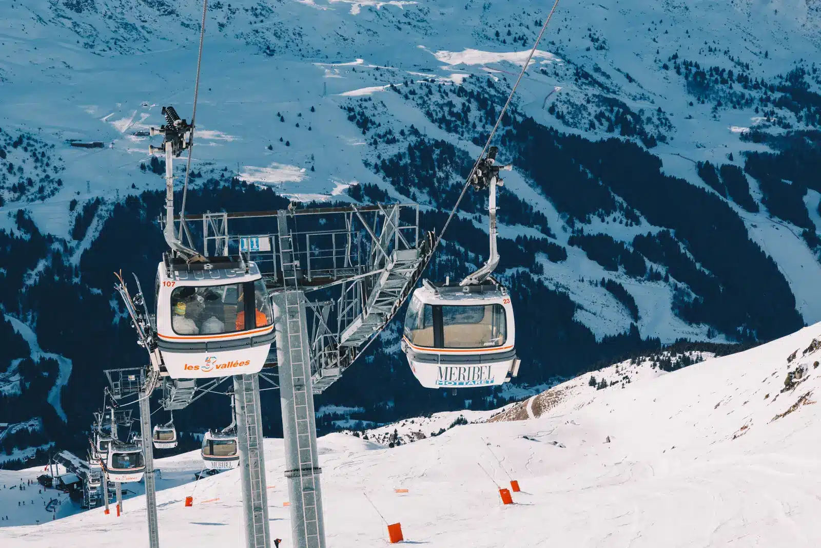 Two ski gondolas travelling above snow-covered mountain slopes