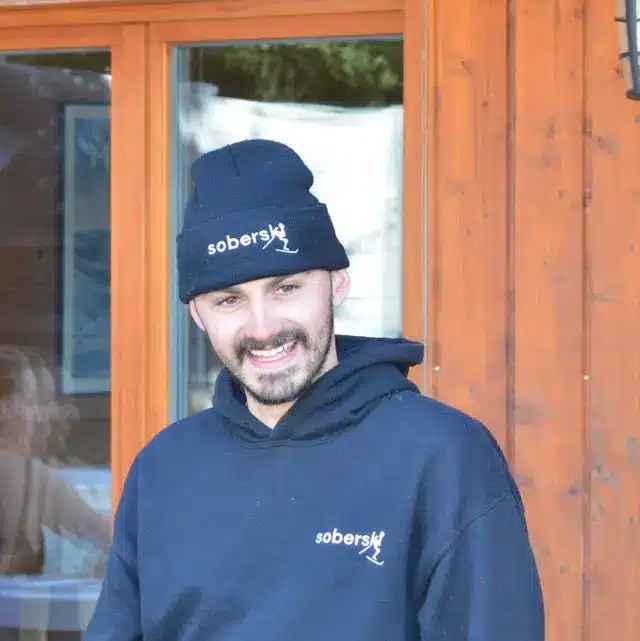 Ben Coombes wearing a Soberski hat outside a wooden chalet